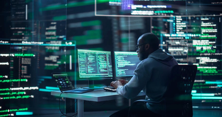 A cybersecurity professional working in a dark room filled with screens displaying code, symbolizing encryption and data security.